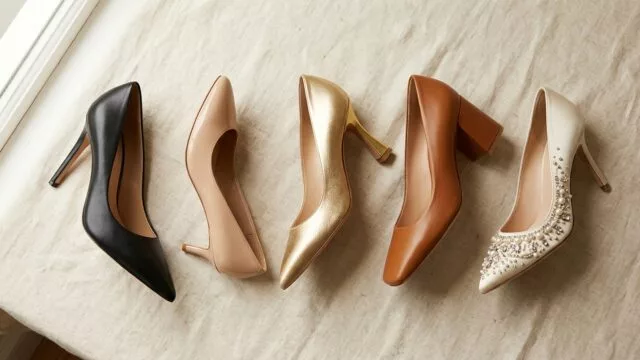 A beautifully arranged flat lay of elegant women's pump heels in various styles displayed on a soft neutral background — including a classic black pointed-toe stiletto, a nude kitten heel, a metallic gold satin pump, a square-toe block heel in caramel brown, and an embellished pump with pearl details. The shoes are artfully positioned to showcase their distinct heel shapes and toe designs. Soft, natural studio lighting with gentle shadows highlights the texture of genuine leather and satin materials. The overall mood is sophisticated, editorial, and timeless, evoking high-end fashion photography with a warm, refined color palette of black, nude, gold, and cream tones.