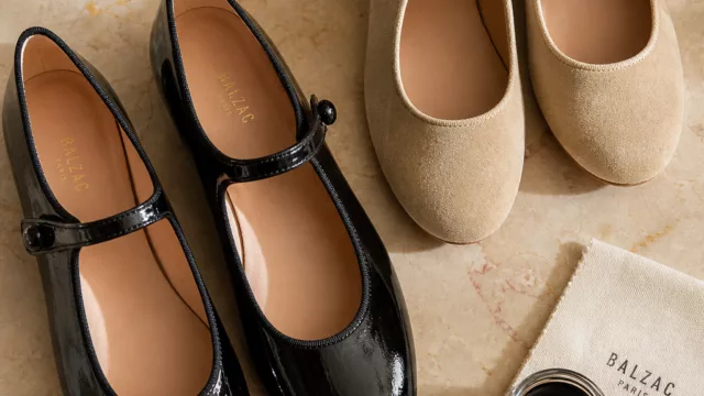 A beautifully styled editorial flat-lay featuring classic Mary Jane shoes in black patent leather and warm beige suede, arranged elegantly on a soft warm-toned marble surface with gentle natural light casting subtle shadows. The shoes showcase their iconic single ankle strap detail with a delicate button closure and rounded toe silhouette. Surrounding the shoes are a few scattered accessories — a small jar of leather polish, a soft cloth, and delicate pearl details — suggesting timeless care and craftsmanship. The composition is clean, sophisticated, and editorial in style, with rich textures and vibrant yet warm tones evoking a sense of enduring elegance and fashion heritage. Realistic product photography aesthetic with a shallow depth of field.