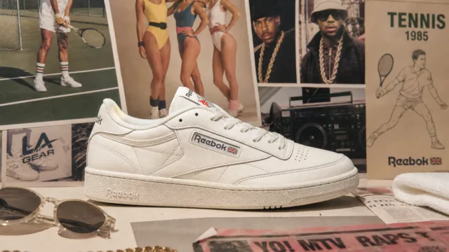 A classic white leather sneaker displayed prominently on a clean minimal surface, surrounded by subtle visual references to athletic heritage — a worn tennis court texture in the background, faint echoes of 1980s aerobics culture, street style fashion, and hip-hop imagery blending together in a collage-like composition. The overall mood is nostalgic yet modern, with soft warm lighting highlighting the timeless simplicity of the sneaker's design. The color palette features crisp whites, muted creams, and soft shadows, evoking both retro elegance and contemporary streetwear culture. Editorial fashion photography style with a lifestyle aesthetic.